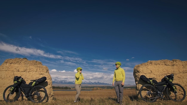 De man en vrouw reizen op gemengd terrein fietstochten met bikepacking. De twee mensen reizen met fietstassen. Berg met sneeuw bedekte, stenen boog.