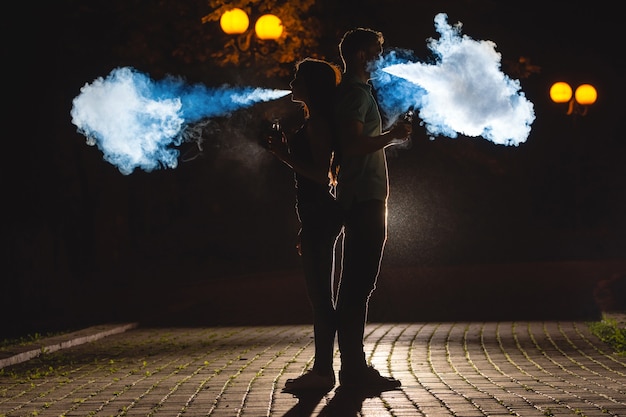 Foto de man en vrouw roken een elektrische sigaret op de donkere straat. nachttijd