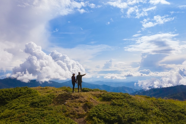 De man en vrouw staan op een berg tegen prachtige wolken