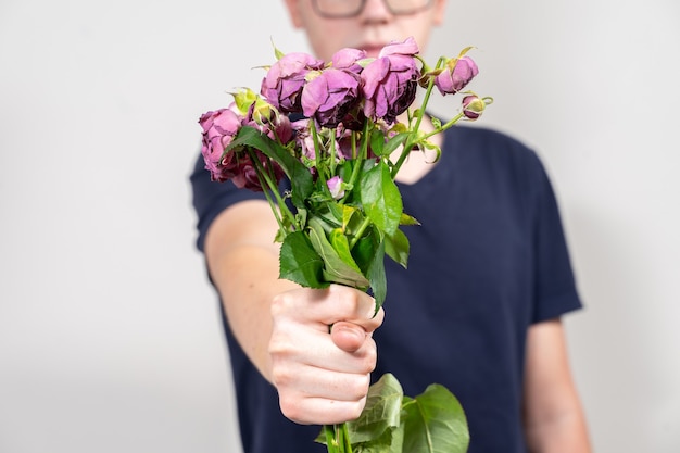 De man houdt een boeket van dode en verdorde bloemen vast en toont fig