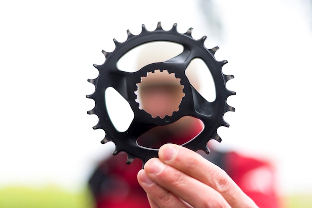 Foto de man houdt een fiets met smalle wiade kettingblad in zijn hand. de man is wazig op de achtergrond.