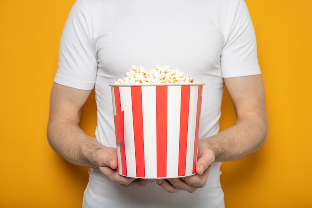 De man houdt popcorn in zijn handen op een gele muur. plaats voor tekst.