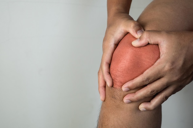 Foto de man houdt zijn pijnpunt van het kniegewricht vast het rode punt toont de positie van de verwonding vooraanzicht close-up shot