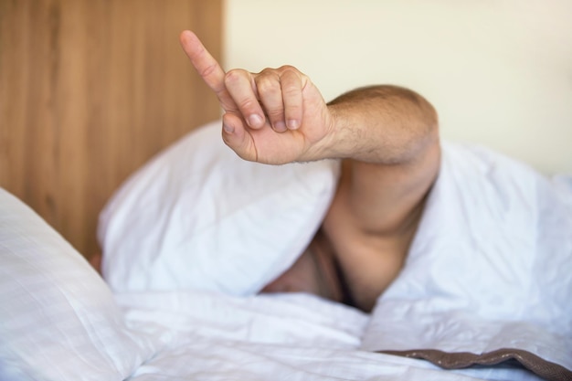 De man in bed verborg zijn hoofd onder het kussen en wil niet wakker worden