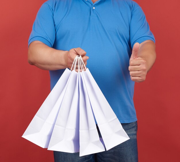 De man in blauwe kleren houdt een stapel witte papieren zakken vast, een andere hand toont als een gebaar