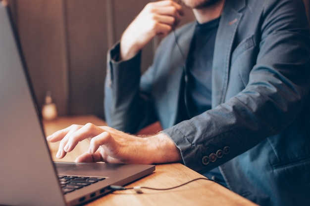 De man in blauwe pak met een koptelefoon op een laptop werkt in het café