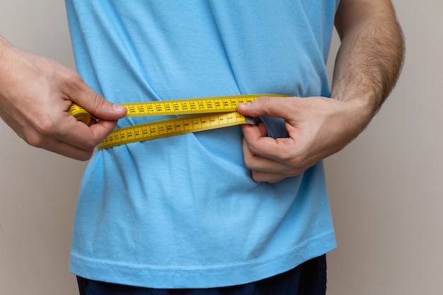 De man in een blauw T-shirt meet de taille met gele tape