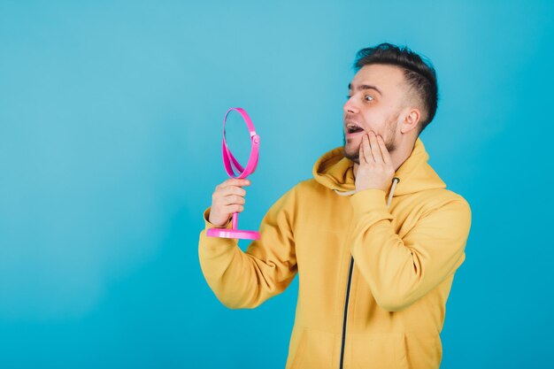 de man in het gele sweatshirt kijkt naar zichzelf in de roze spiegel