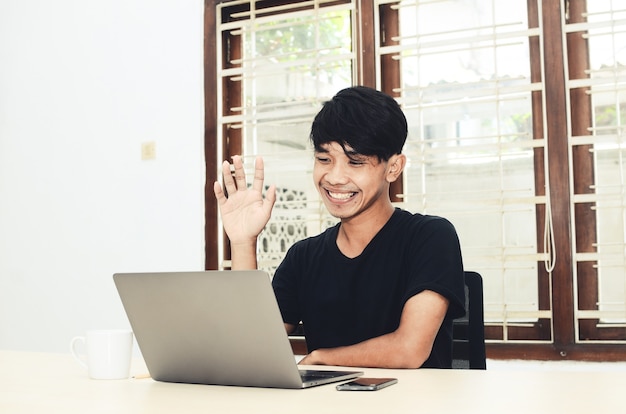 De man in het zwarte Aziatische shirt zat voor de laptop tijdens een videogesprek