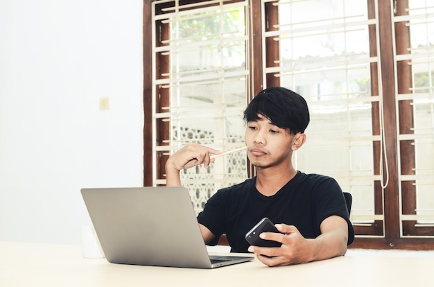 De man in het zwarte Aziatische T-shirt zat met een droevige uitdrukking voor de laptop