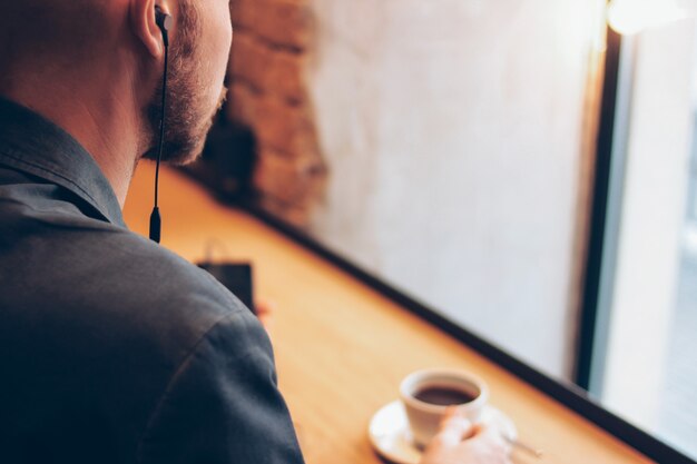 De man in hoofdtelefoons met behulp van mobiele telefoon, zittend met koffie in het café