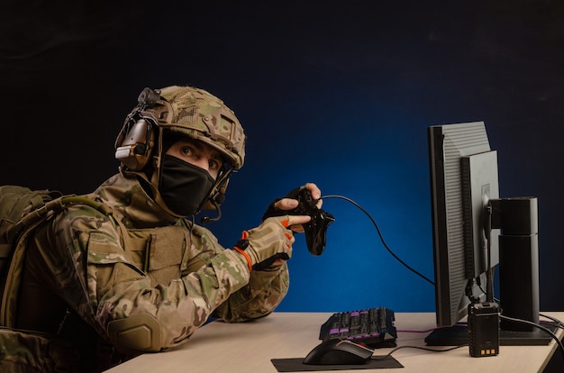 De man in militair uniform zit computerspelletjes te spelen op een computer met een joystick