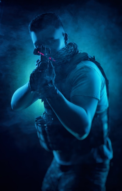 De man in speciale militaire kleding poseert met een pistool in zijn handen op een donkere achtergrond in de nevel