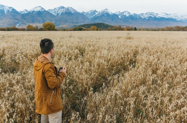 De man is een fotograaf in het veld tegen de achtergrond van bergen maakt een foto op een oude retro filmcamera Man loopt in de herfst in vrijetijdskleding Concept lifestyle millennial hipster