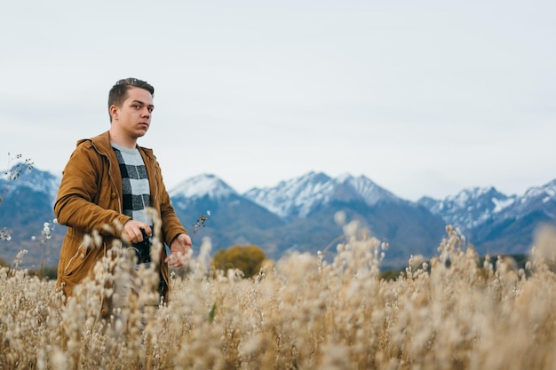 De man is een fotograaf in het veld tegen de achtergrond van bergen maakt een foto op een oude retro filmcamera Man loopt in de herfst in vrijetijdskleding Concept lifestyle millennial hipster