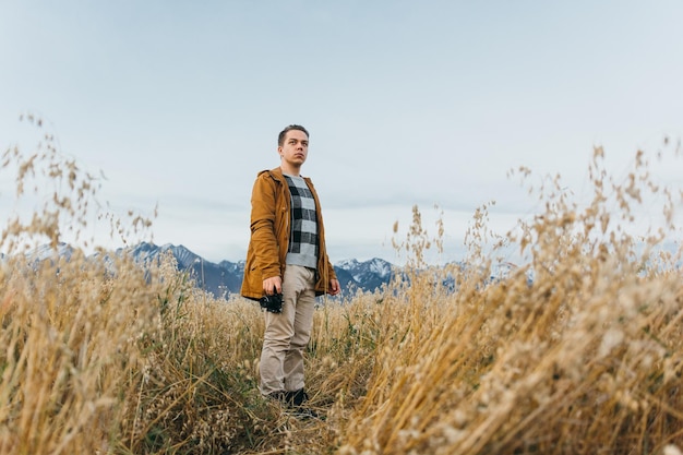 De man is een fotograaf in het veld tegen de achtergrond van bergen maakt een foto op een oude retro filmcamera Man loopt in de herfst in vrijetijdskleding Concept lifestyle millennial hipster