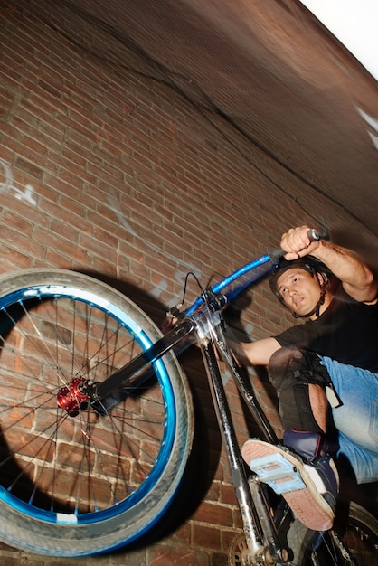 De man is een wielrenner in beweging, rijdend op het achterwiel van de fiets bij de muur van het rode bakstenen gebouw