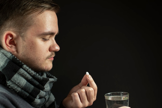 De man is ziek in een sjaal en slikt medicijnen op een jonge volwassene met een donkerwaterpil