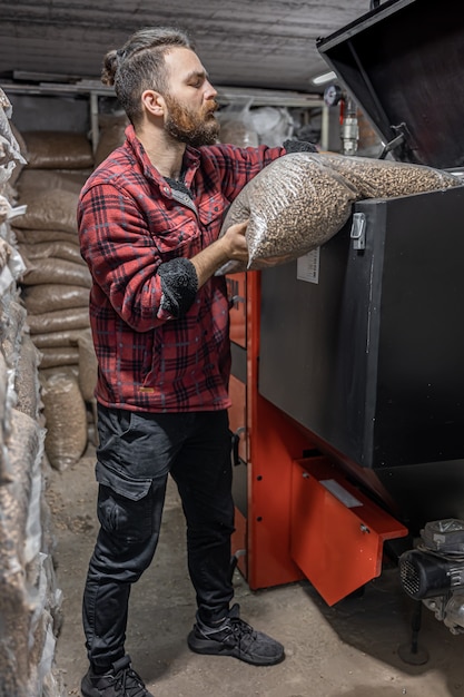 De man laadt de pellets in de vastebrandstofketel, werkend met biobrandstoffen, zuinige verwarming.