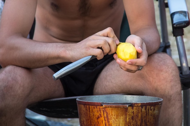 De man maakt aardappelen schoon in een pot in natuurkamp Handen close-up