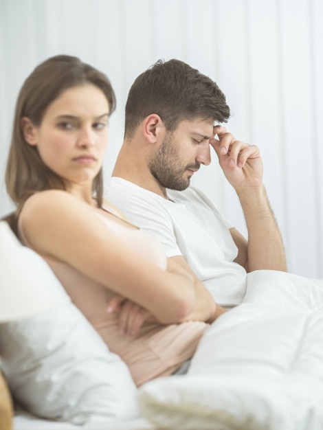 De man met hoofdpijn zit naast de vrouw op het bed