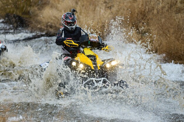 De man op de quad steekt een beek over. Toeristische wandelingen op een langlaufterrein.