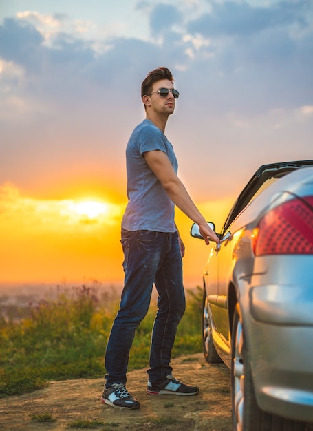 De man opent de deur van een auto op de achtergrond van de felle zon