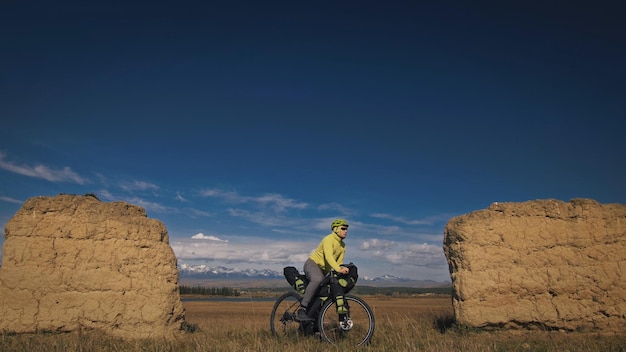 De man reist op gemengd terrein fietstochten met bikepacking De reiziger reis met fietstassen Sport bikepacking fiets sportkleding in groen zwarte kleuren Berg besneeuwde stenen boog