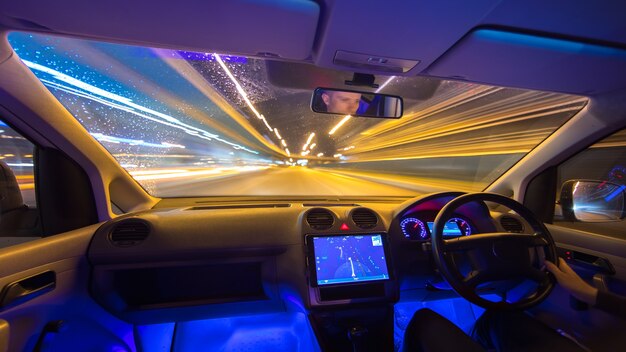 De man rijdt met een navigatie op een regenweg. Links verkeer. Wijde hoek