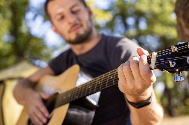 De man speelt gitaarmuziek bij de tent op een klapstoel in het bos