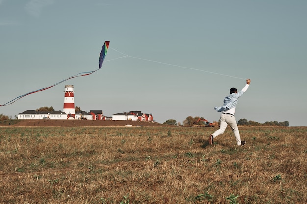 De man speelt met een vlieger in het veld. vuurtoren op de achtergrond. herfsttijd, buitenspellen.