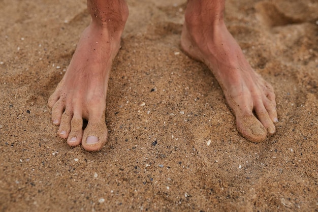 De man staat blootsvoets op het zand Benen close-up Zee Oceaan