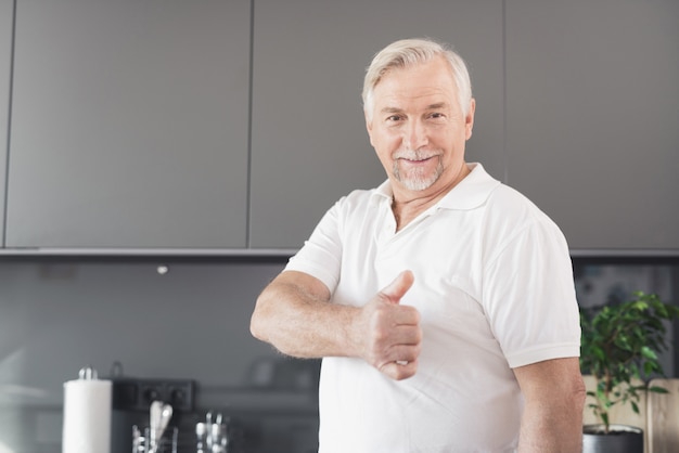 De man staat in de keuken. hij steekt zijn duim op.