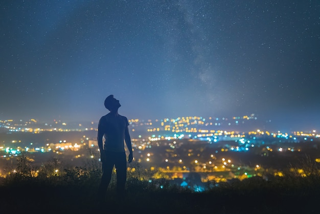 De man staat op de achtergrond van de sterrenhemel boven de nachtstad