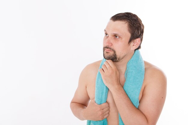 De man streelt zijn baard. ochtendbehandelingen in de badkamer. blauwe handdoek om haar nek. geïsoleerd op een witte achtergrond. kopieer ruimte