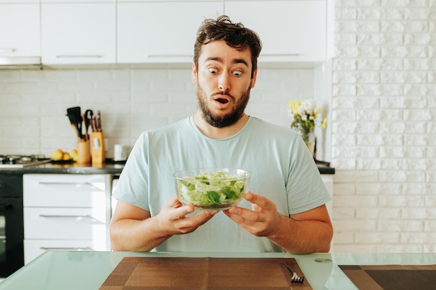 De man trekt een zeer expressief gezicht bij het zien van een salade van groenten met een kom in zijn handen