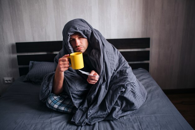 De man werd ziek. Ligt in bed en lijdt. Hij heeft koorts, griep, verkoudheid en snot.