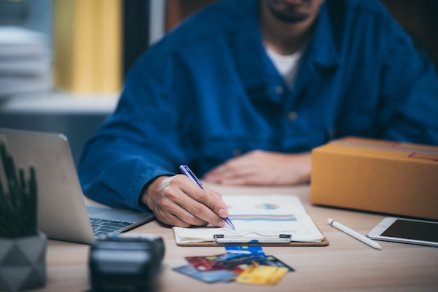 De man werkende laptop computer van huis op houten vloer met postpakket, die online ideeënconcept verkopen.