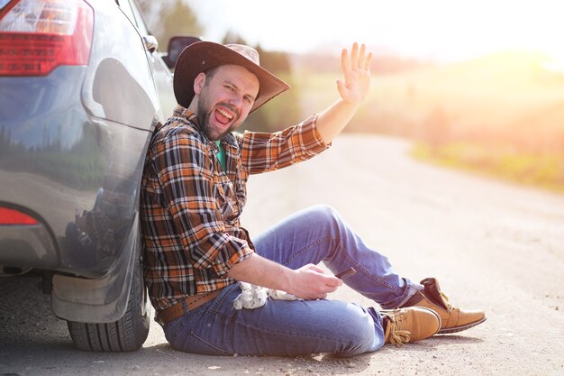 De man zit op de weg bij de auto in de natuur