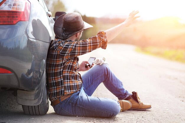 De man zit op de weg bij de auto in de natuur