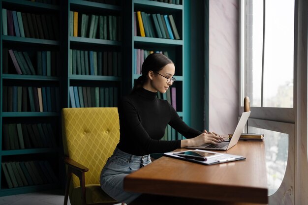 De manager is een vrouw met een bril die in een coworking-ruimte op kantoor werkt, een laptop gebruikt en een bedrijfsrapport maakt over een videogesprek