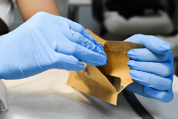 De manicuremeester opent de steriele instrumenten. handen met blauwe handschoenen openen het pakket.