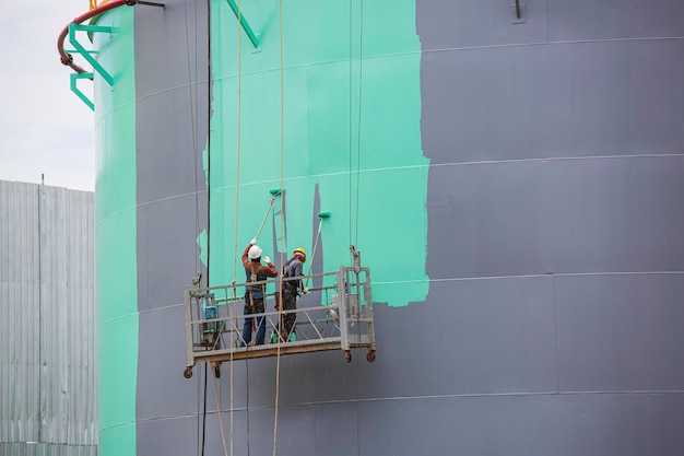 De mannelijke arbeider neemt de kabelbaan met een industriële schilderborstel die wordt gebruikt voor schaalplaattankolieoppervlakte groene kleur