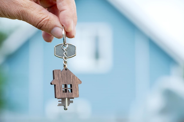 De mannelijke hand van een makelaar houdt de sleutels van het huis op de achtergrond van een landhuis