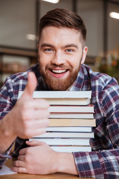 De mannelijke stapel van de studentenholding boeken terwijl het zitten in bibliotheek