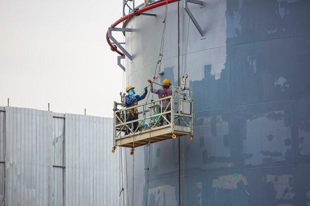 De mannelijke werknemer met een industriële verfborstel die wordt gebruikt voor het olieoppervlak van de schaalplaat, is grijs geverfd