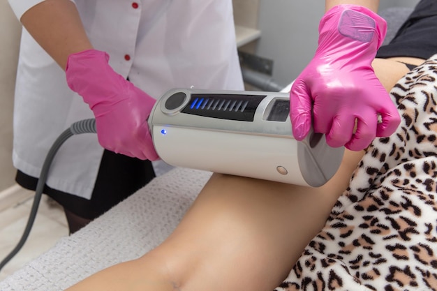 De masseur doet een massage met behulp van een anticellulitis-massageapparaat met compressie- en vibratietechnologie in het schoonheidssalon