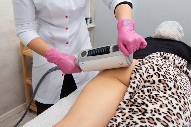 De masseur doet een massage met behulp van een anticellulitis-massageapparaat met compressie- en vibratietechnologie in het schoonheidssalon