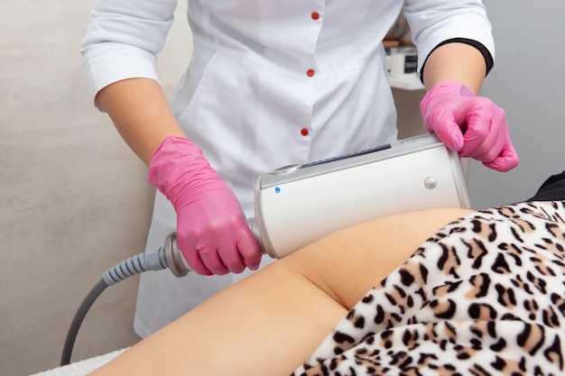 De masseur doet een massage met behulp van een anticellulitis-massageapparaat met compressie- en vibratietechnologie in het schoonheidssalon