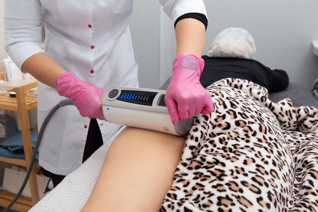De masseur doet een massage met behulp van een anticellulitis-massageapparaat met compressie- en vibratietechnologie in het schoonheidssalon